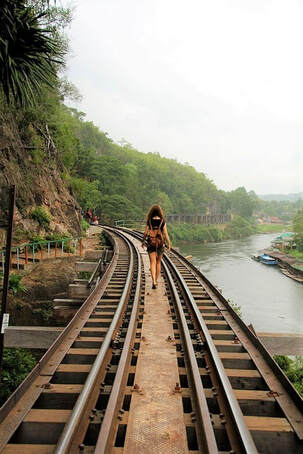 woman walking in middle of train tracks with river on her right hand side